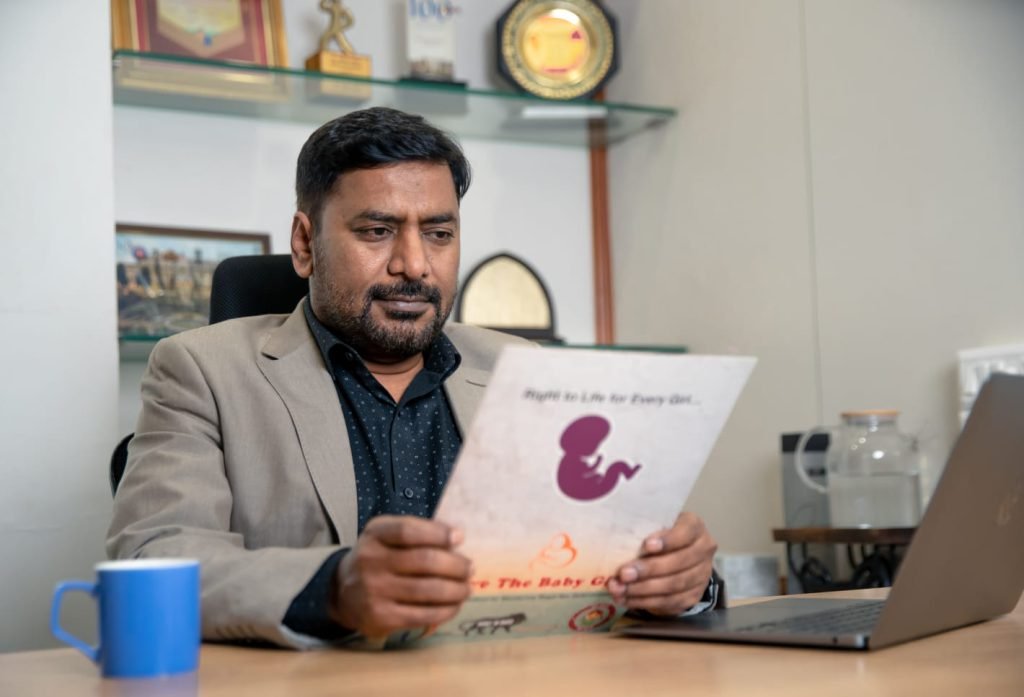 Dr. Girish Lad seated at his desk, reading a Save the Baby Girl publication